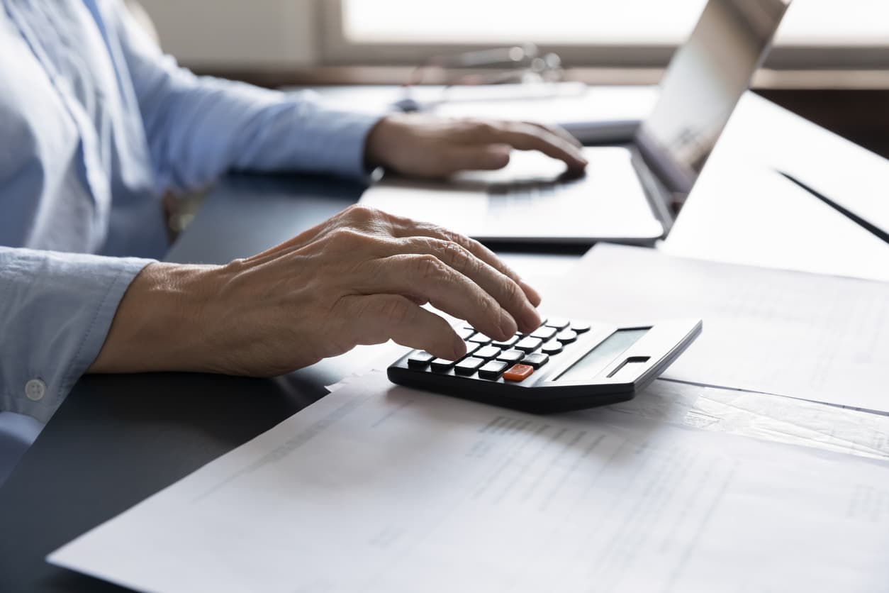 Computing costs of drafting a will. Senior man using a calculator while computing the cost of a will.